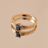 An emerald cut blue sapphire set in a yellow gold ring with hand engraved botanical details on the band